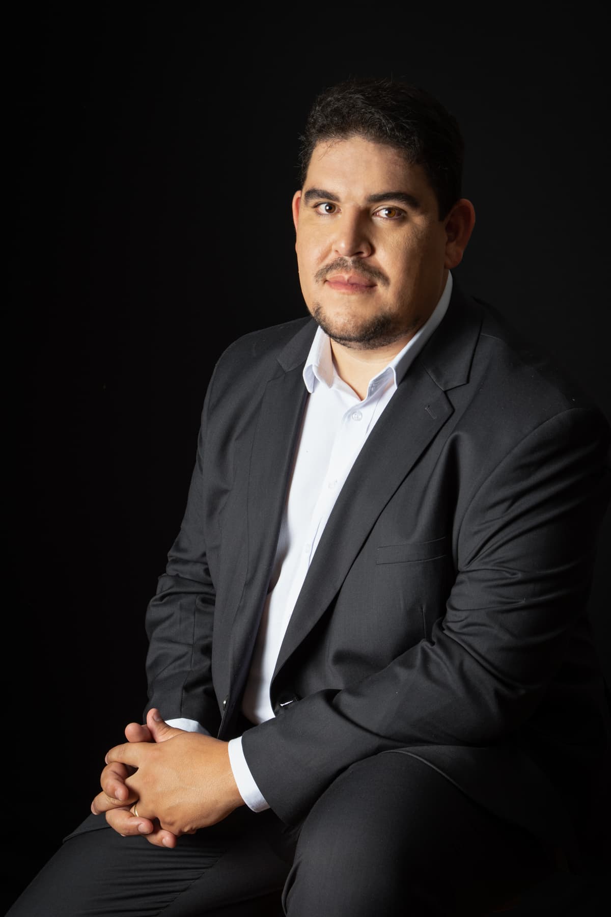 Ítalo Samuel Cardoso de Jesus, de terno, sentado, em fundo escuro